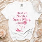 White t-shirt with pink text and graphic of "This Girl Needs a Spicy Marg" cocktail.