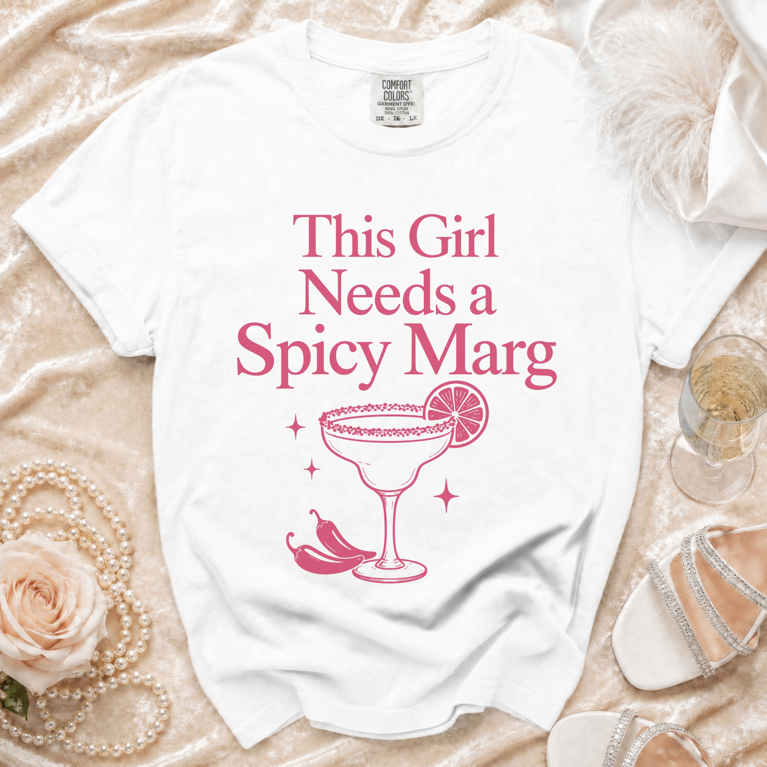 White t-shirt with pink text and graphic of "This Girl Needs a Spicy Marg" cocktail.