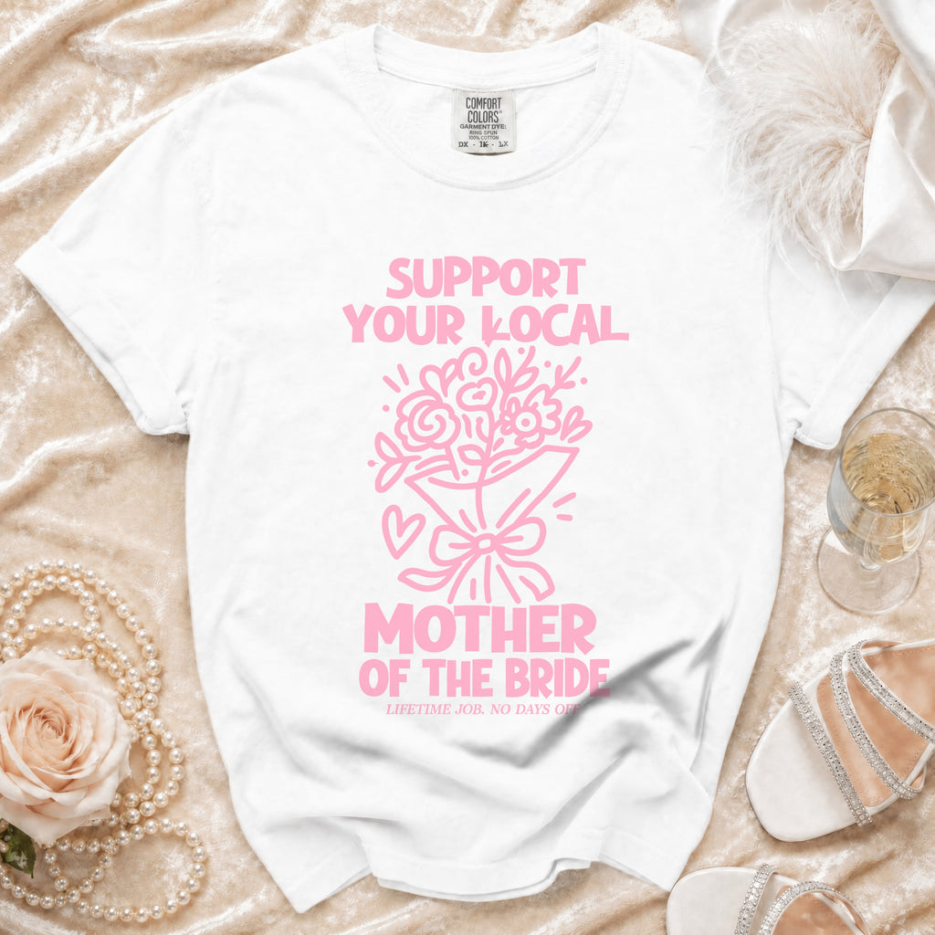 White t-shirt with pink text "SUPPORT YOUR LOCAL MOTHER OF THE BRIDE" and flower bouquet graphic.