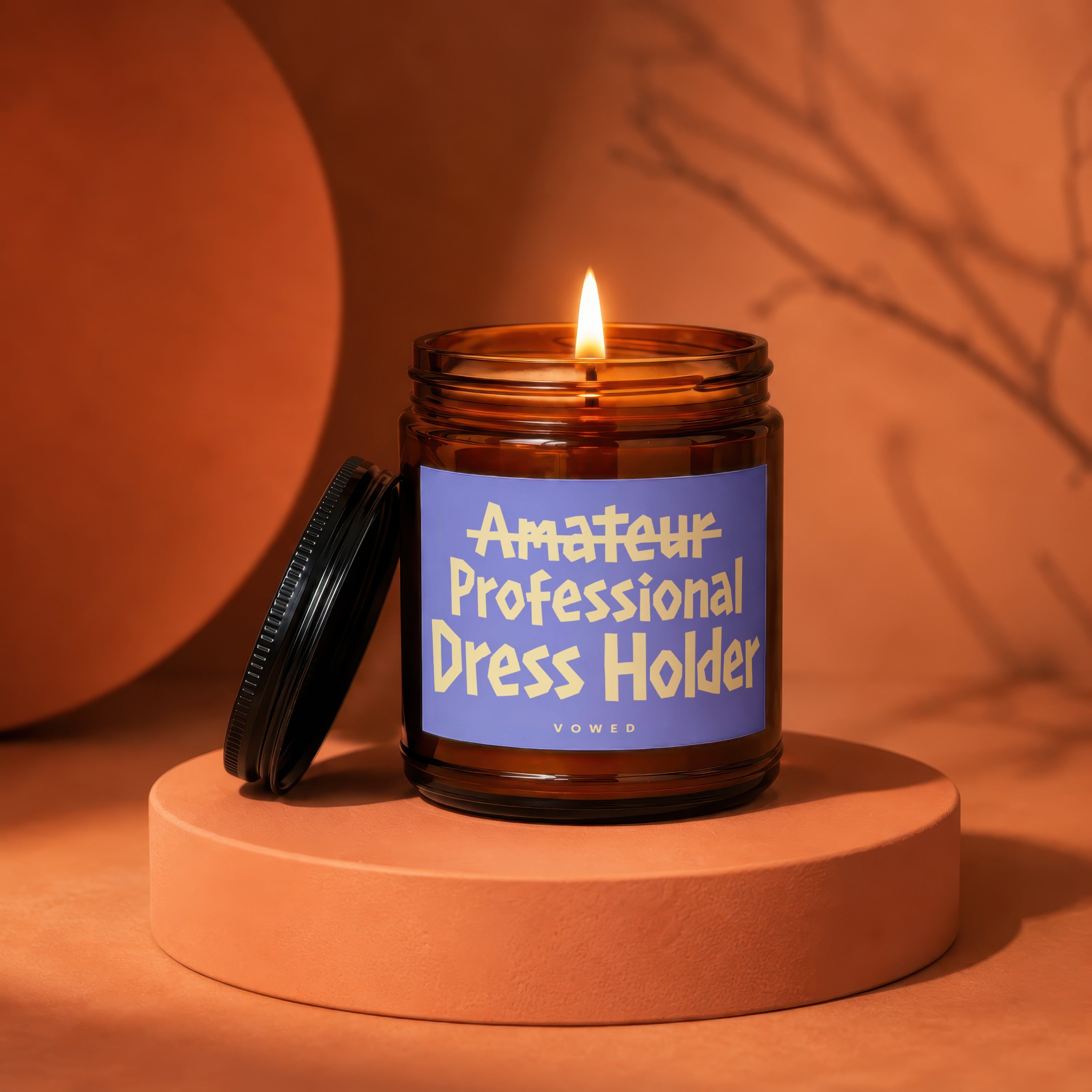 Amber candle jar with lit flame on an orange pedestal, with text "Amateur Professional Dress Holder".
