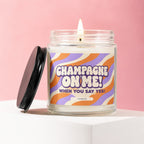 Glass candle with burning wick, featuring "Champagne On Me!" text.