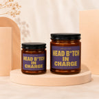 Two amber glass candles with purple labels reading "Smells Like Head B*tch In Charge".