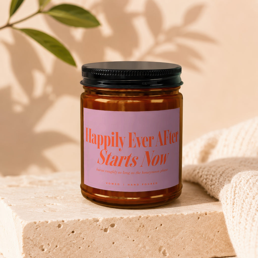 Brown glass candle with pink label reading "Happily Ever After Starts Now."