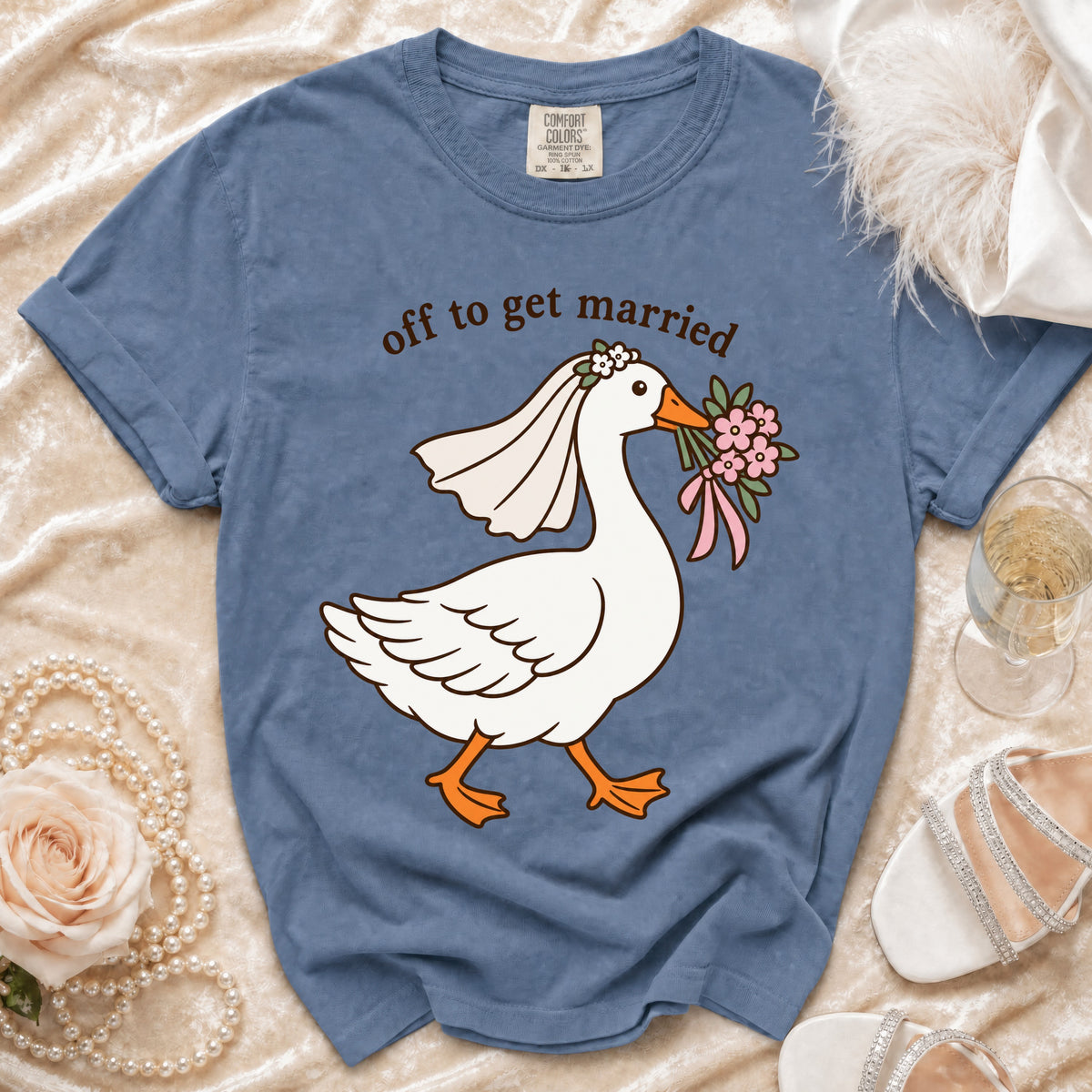 Blue t-shirt with a goose wearing a veil and holding flowers, text "off to get married".