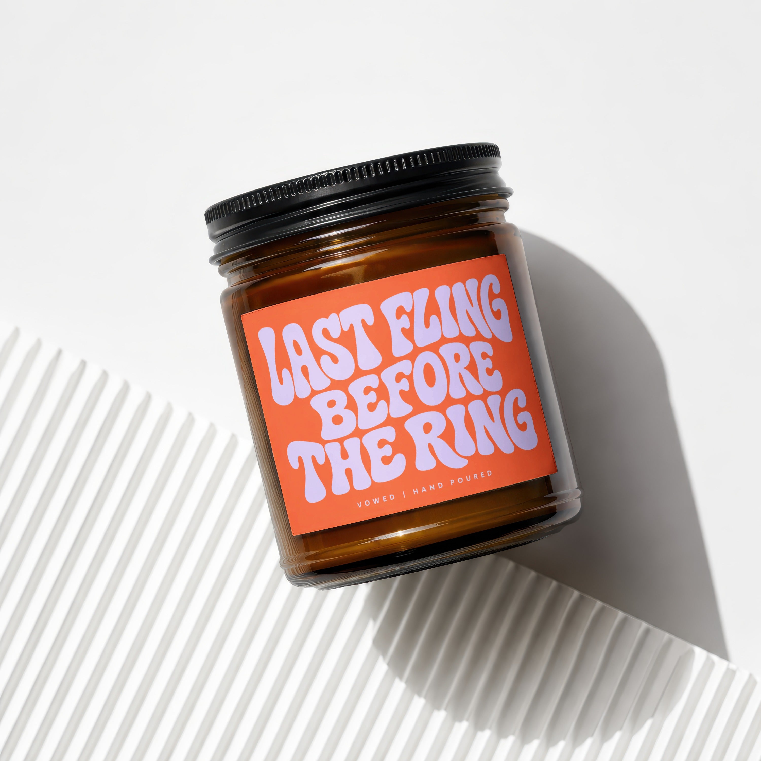 Brown glass candle in a black lid with an orange label reading "LAST FLING BEFORE THE RING".