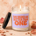 Lit candle with lavender label reading "Two Brides Are Better Than One" and "Love Wins, Always."