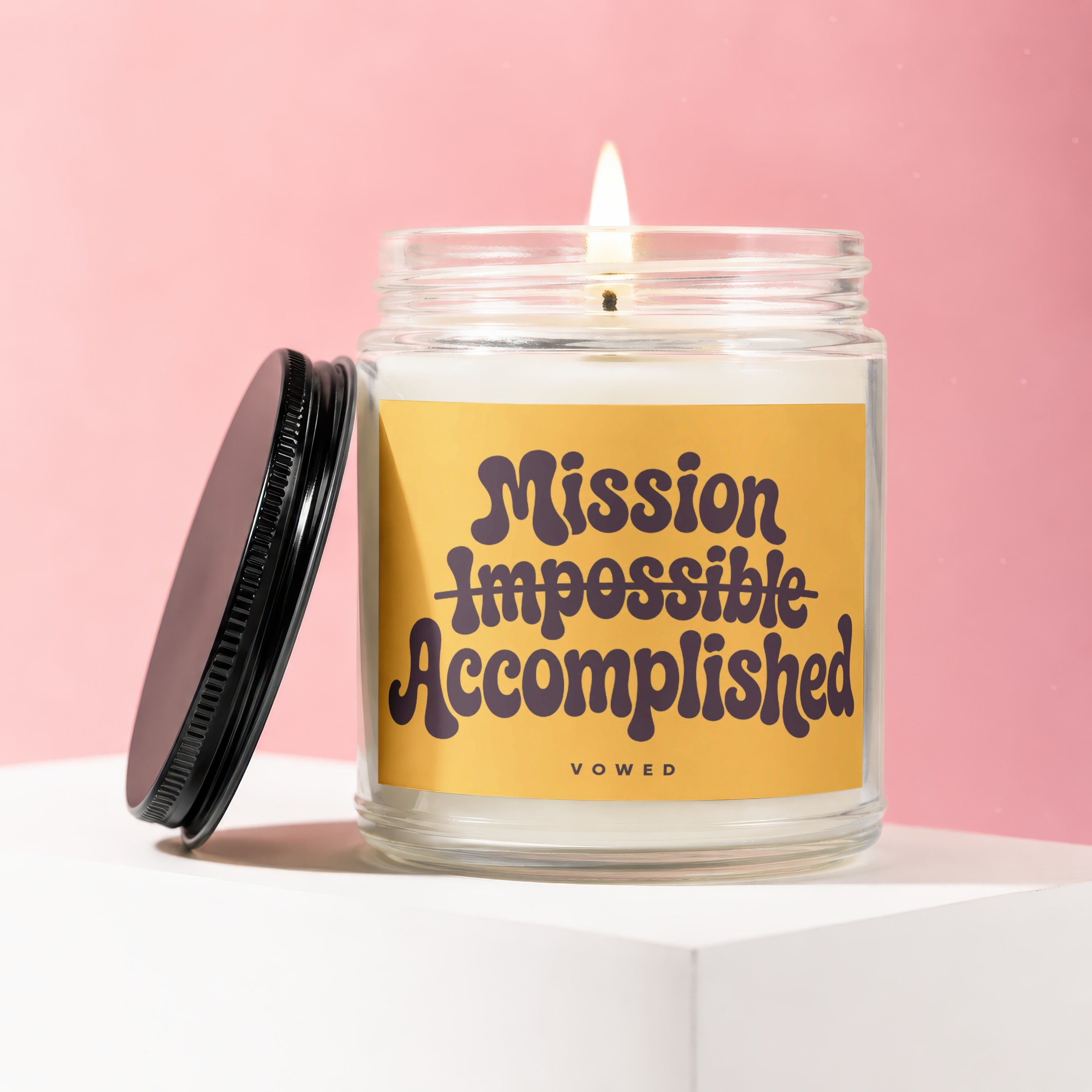 Lit candle in glass jar with yellow label that reads "Mission Impossible Accomplished"