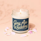 Lit candle in jar with navy label reading "Gay Ass Wedding Vowed" surrounded by petals.