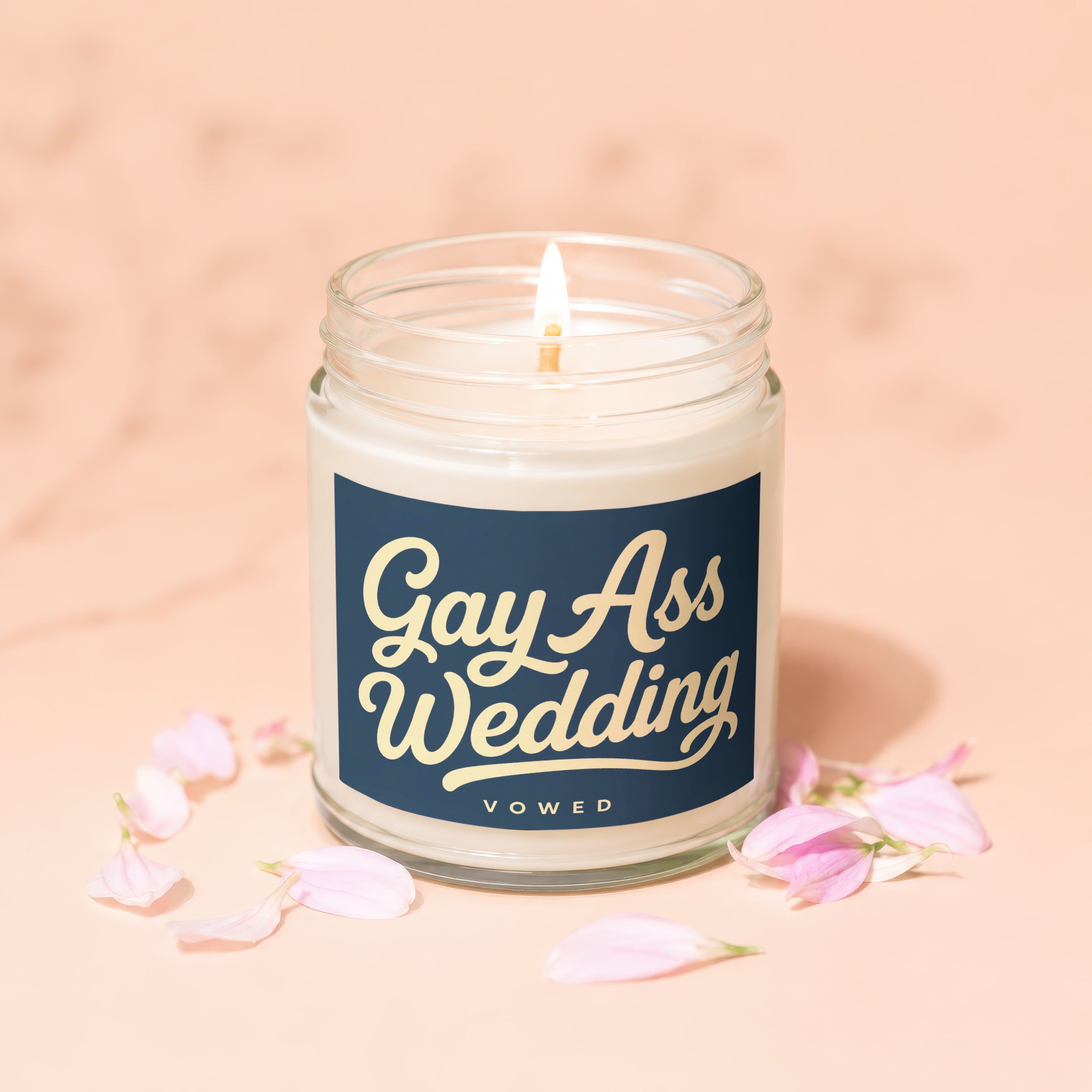 Lit candle in jar with navy label reading "Gay Ass Wedding Vowed" surrounded by petals.
