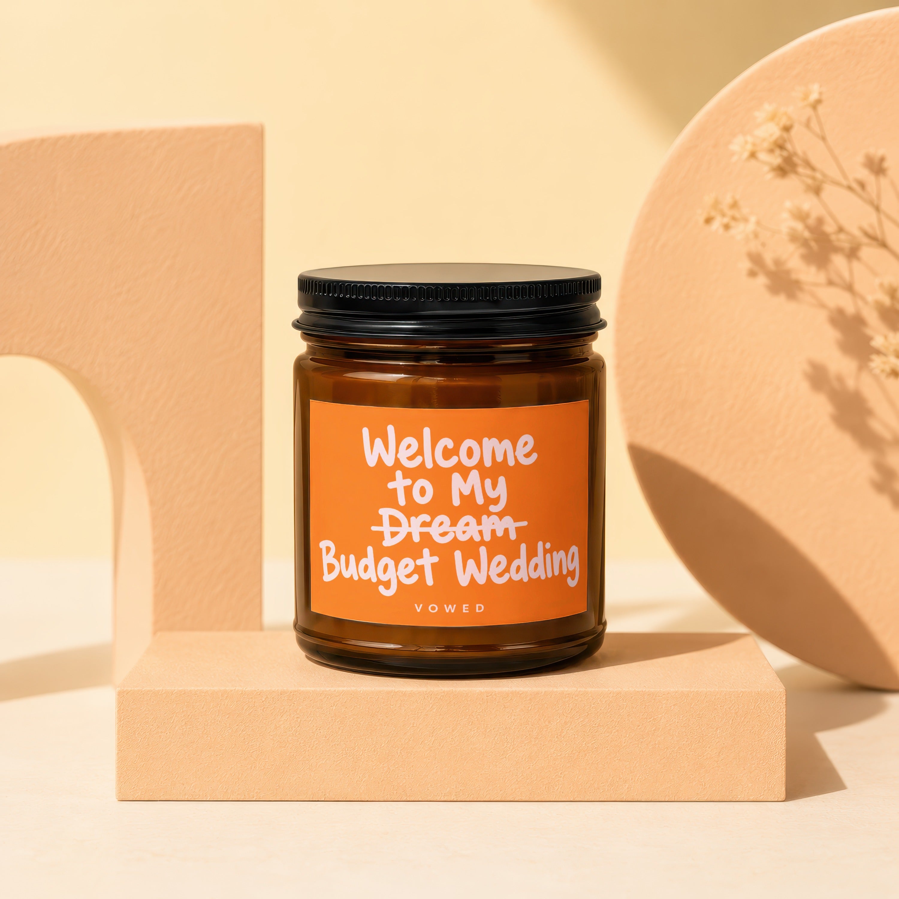 Brown candle with orange label reading "Welcome to My Dream Budget Wedding VOWED".