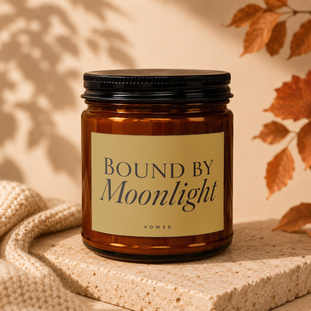 Amber candle with "Bound By Moonlight" on a golden label, with autumn leaves and knit fabric.