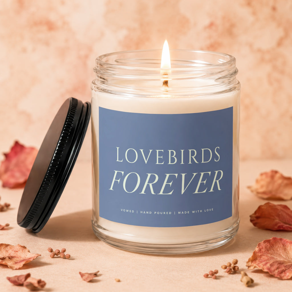 Glass jar candle lit with blue label reading "Lovebirds Forever."