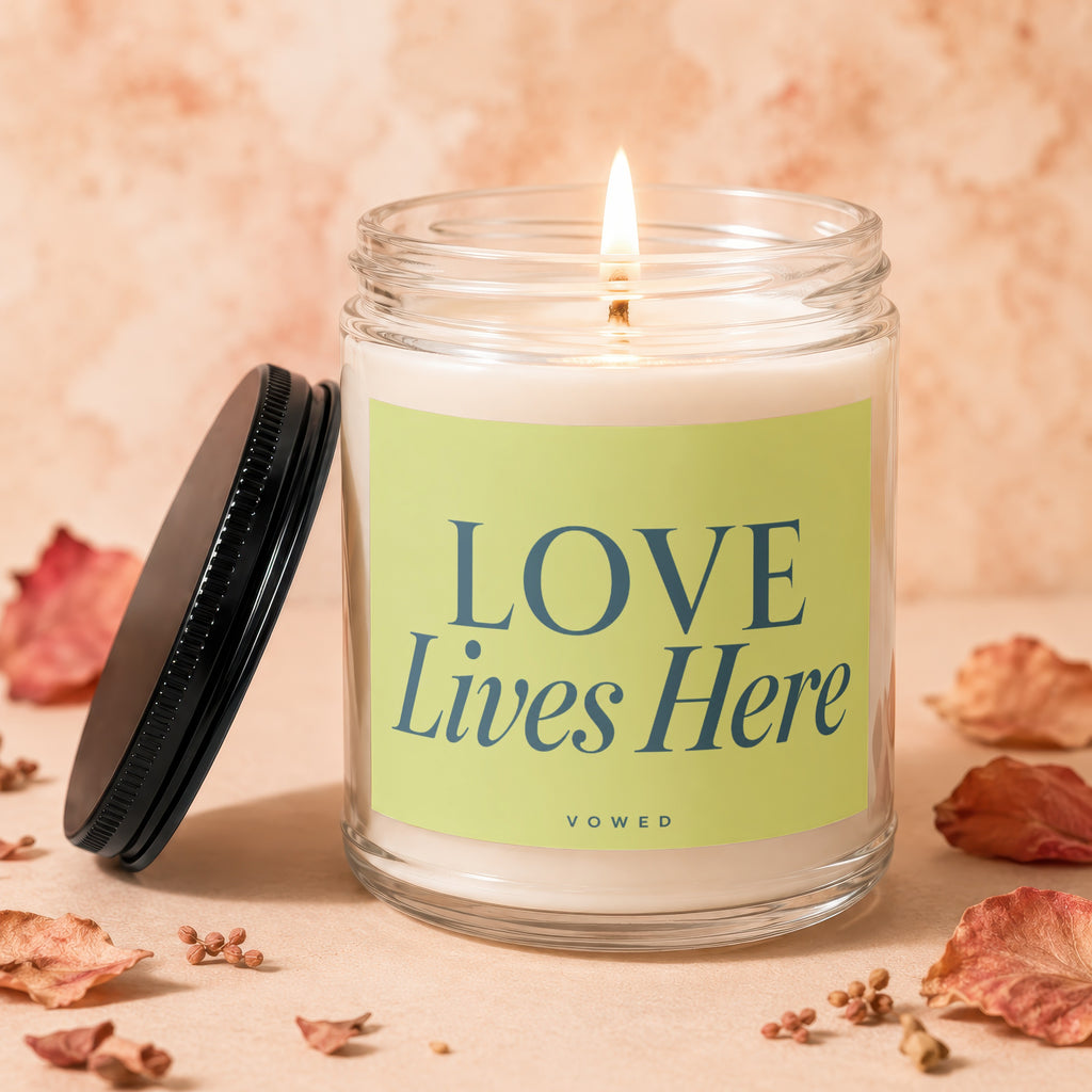 Candle with lit wick, green label reading "LOVE Lives Here" and "VOWED".