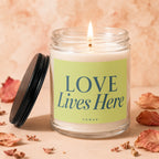 Candle with lit wick, green label reading "LOVE Lives Here" and "VOWED".