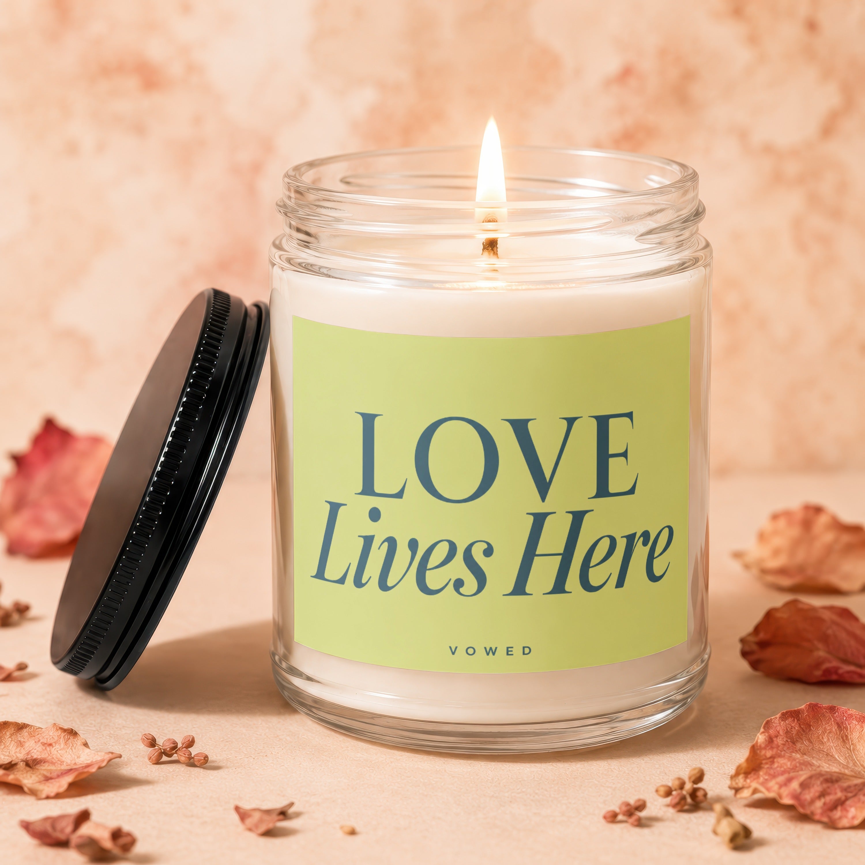 Candle with lit wick, green label reading "LOVE Lives Here" and "VOWED".