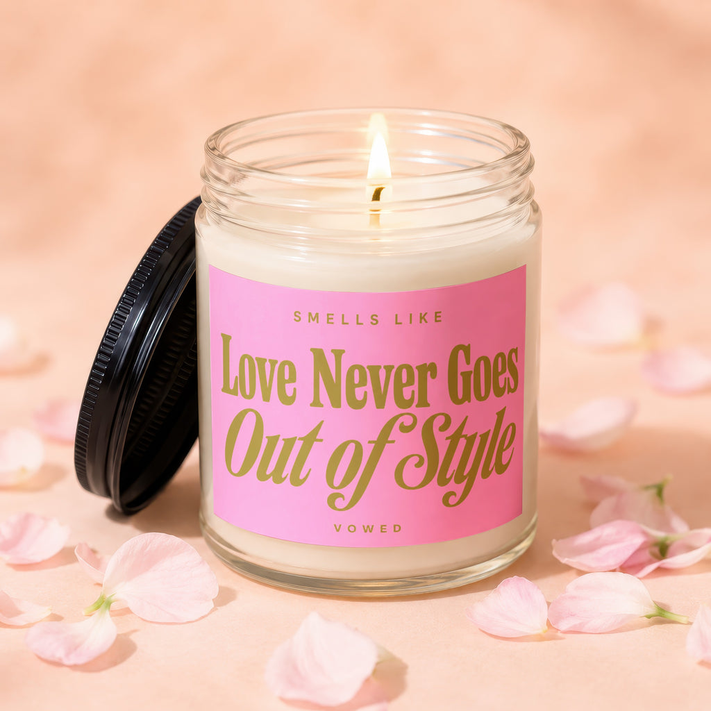 Lit glass jar candle with pink label reading "Smells Like Love Never Goes Out of Style Vowed".