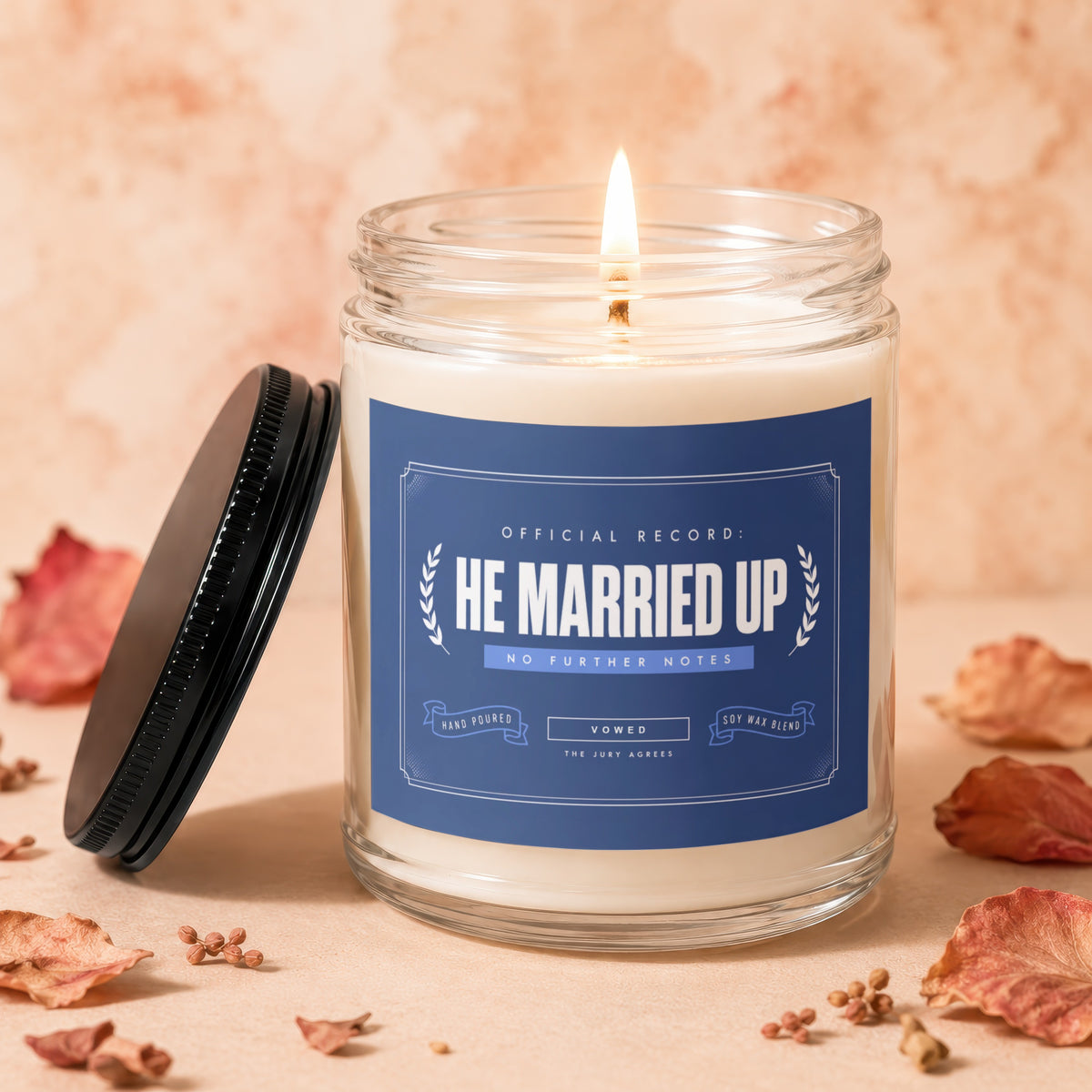 Lit candle in glass jar with blue label reading "HE MARRIED UP".