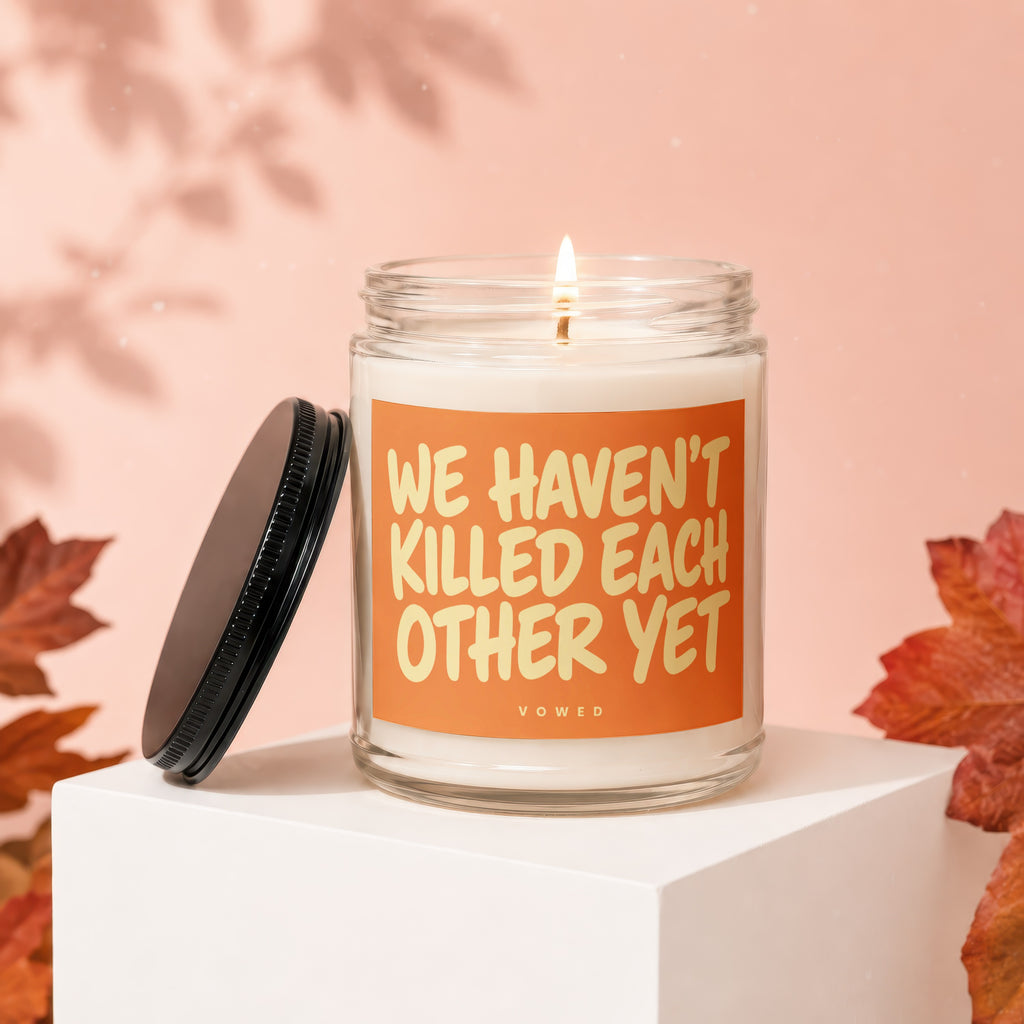 Glass candle with orange label that reads "WE HAVEN'T KILLED EACH OTHER YET".
