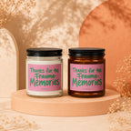 Two candles with pink labels saying "Thanks for the Trauma Memories" on a light orange pedestal.