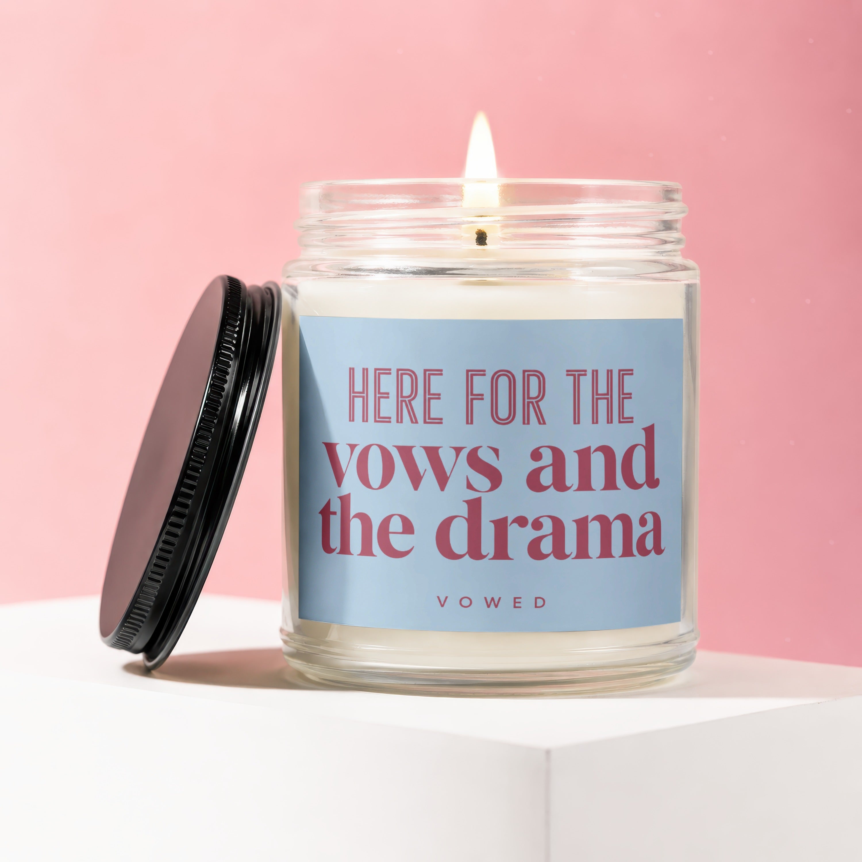 Lit candle in glass jar with lid ajar, label reads "HERE FOR THE vows and the drama".