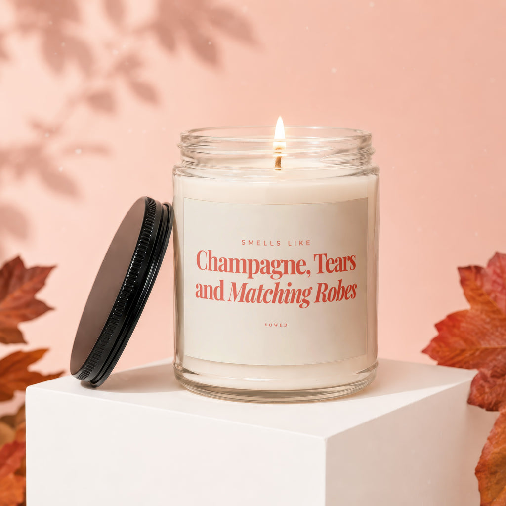 Lit candle in glass jar with label: "Smells like Champagne, Tears and Matching Robes."