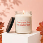 Lit candle in glass jar with label: "Smells like Champagne, Tears and Matching Robes."