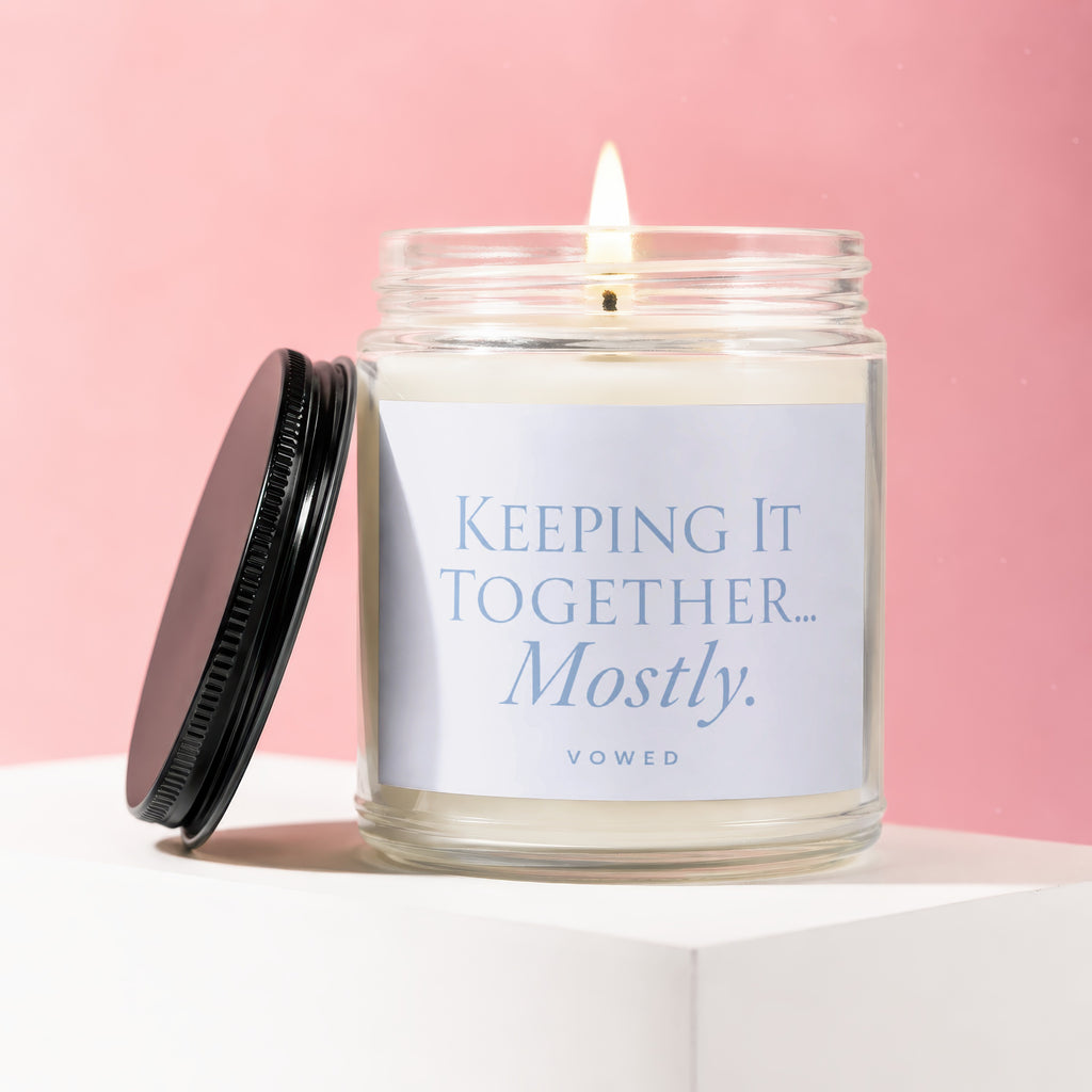 Glass candle with lid off, "KEEPING IT TOGETHER... Mostly." text on label.