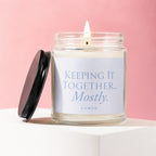 Glass candle with lid off, "KEEPING IT TOGETHER... Mostly." text on label.