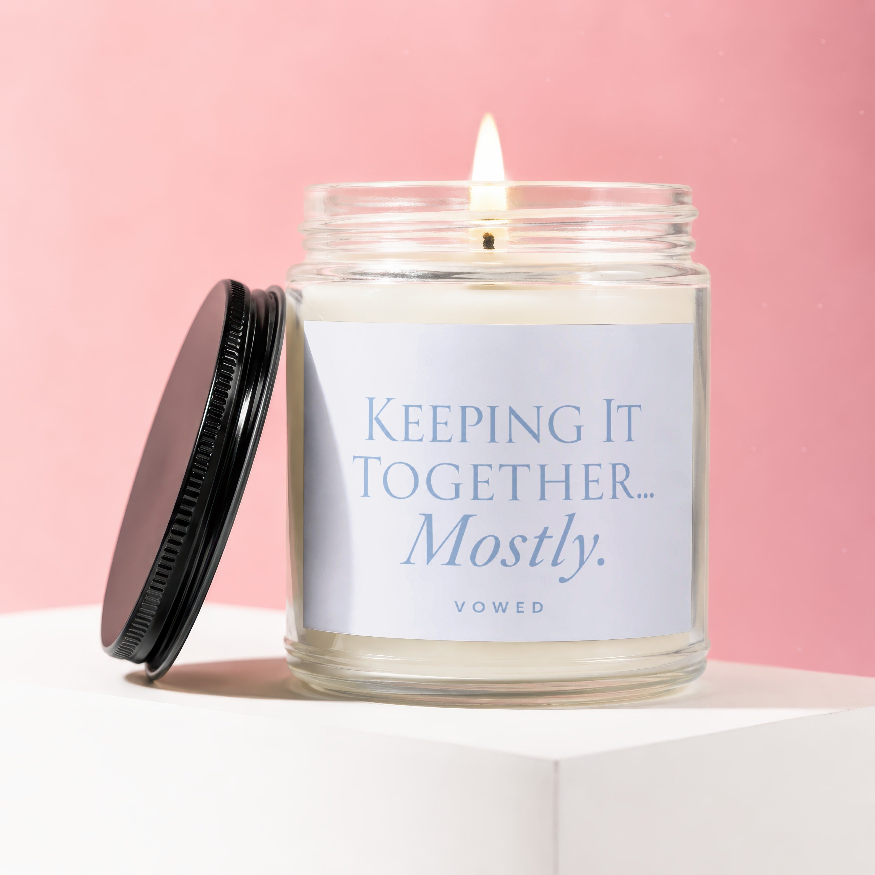 Glass candle with lid off, "KEEPING IT TOGETHER... Mostly." text on label.
