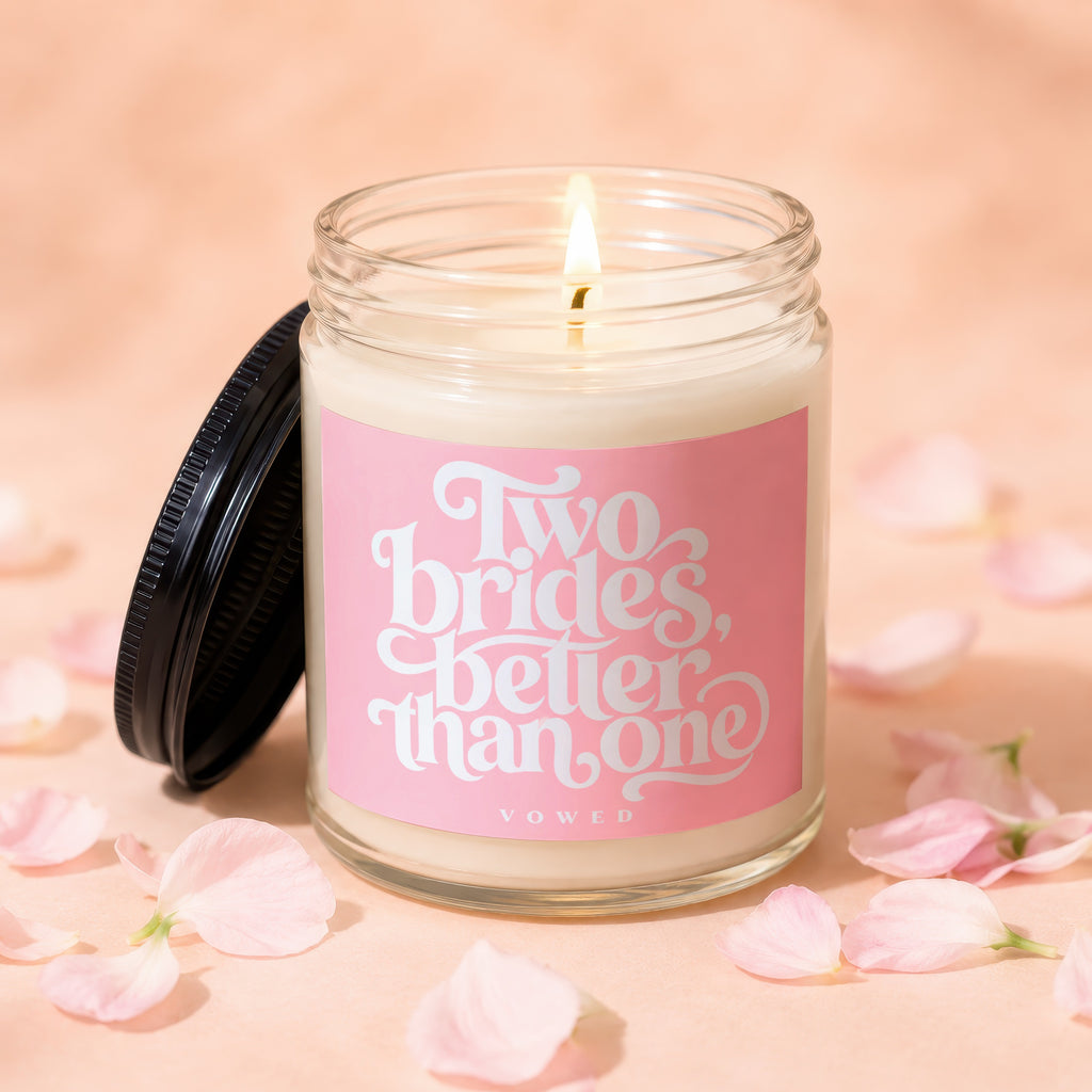 Candle with pink label reading "Two brides, better than one" surrounded by petals.