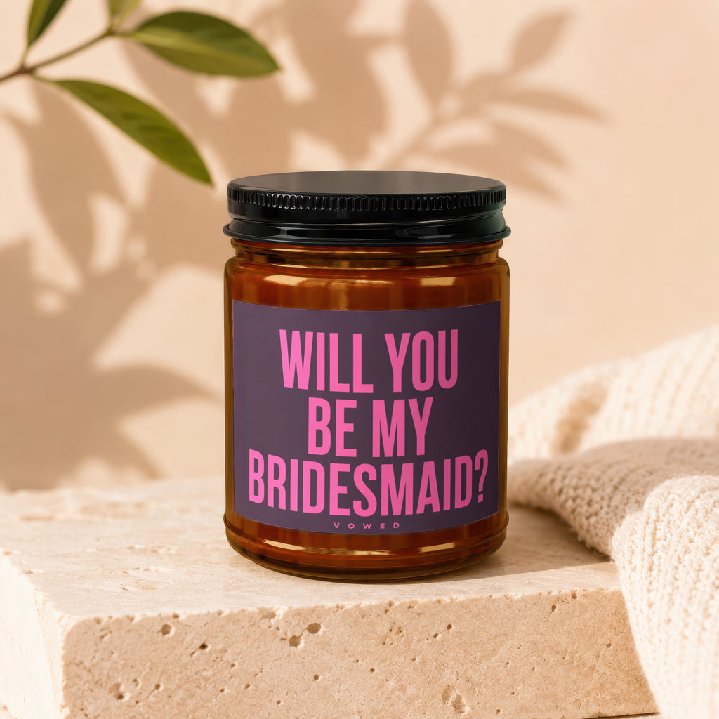 Amber jar candle with dark lid and purple label that reads "Will You Be My Bridesmaid?"