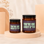 Two amber jar candles with black lids, labeled "YOU'RE ONE LUCKY B*TCH".