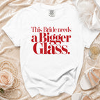 White t-shirt with red text "This Bride needs a Bigger Glass."