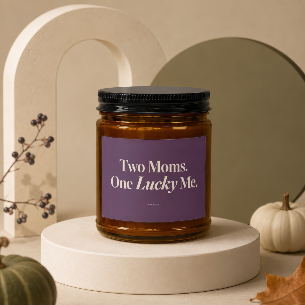 Amber candle in glass jar with purple label reading "Two Moms. One Lucky Me."