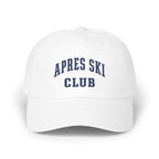 A white baseball cap featuring blue embroidered text that reads APRES SKI CLUB across the front panels.