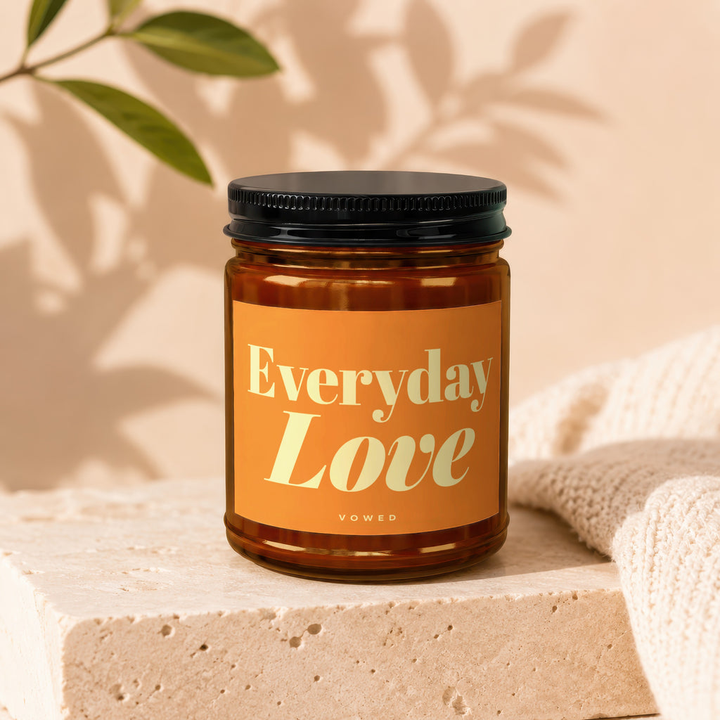 Amber glass candle labeled "Everyday Love" by Vowed on a stone block with a beige knit fabric.