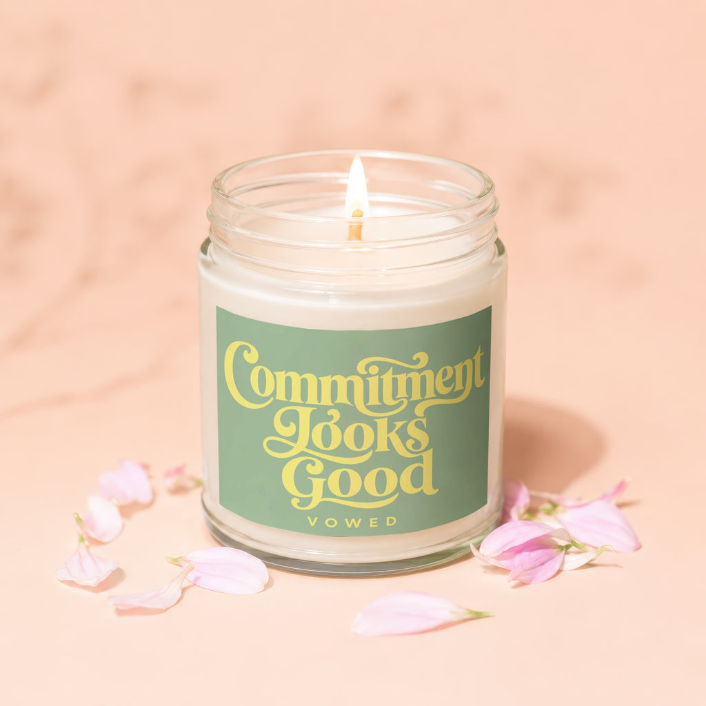Glass jar candle with lit wick and green label reading "Commitment Looks Good."
