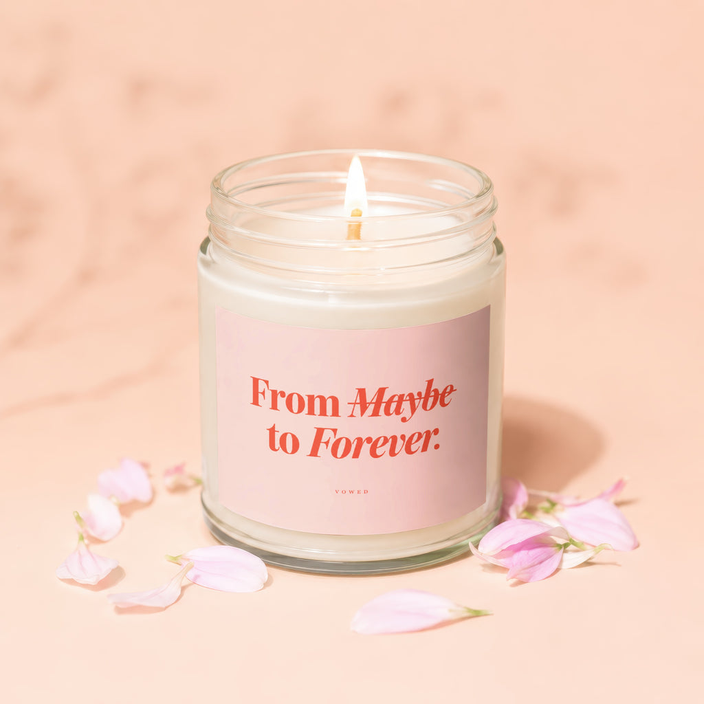 Lit candle in a jar with pink label that reads "From Maybe to Forever. VOWED."