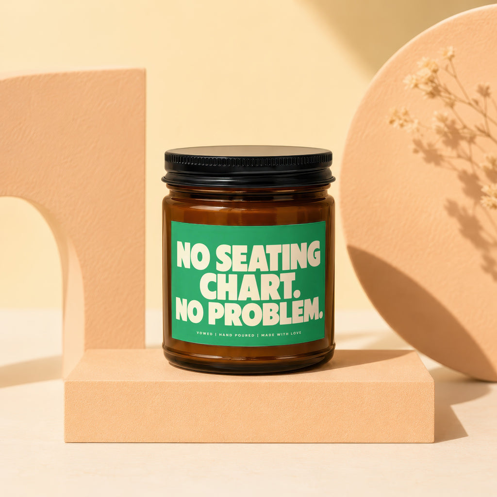 Brown candle in amber glass jar with black lid, green label reads "NO SEATING CHART. NO PROBLEM."