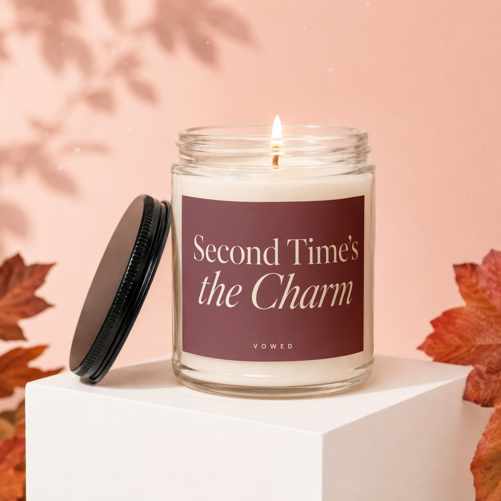 Lit candle in glass jar with dark label reading "Second Time's the Charm" and "Vowed".