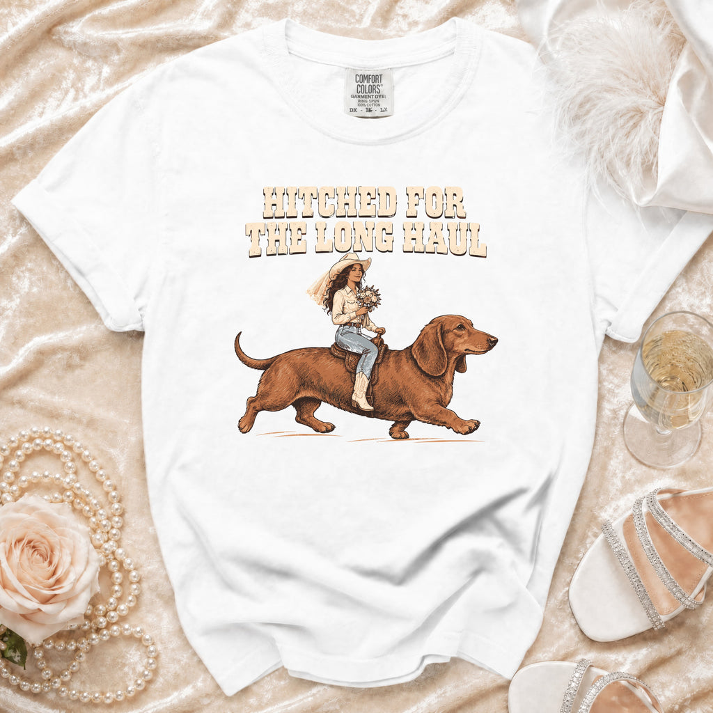 White t-shirt with illustration of a bride riding a dachshund, text reads "Hitched for the Long Haul".