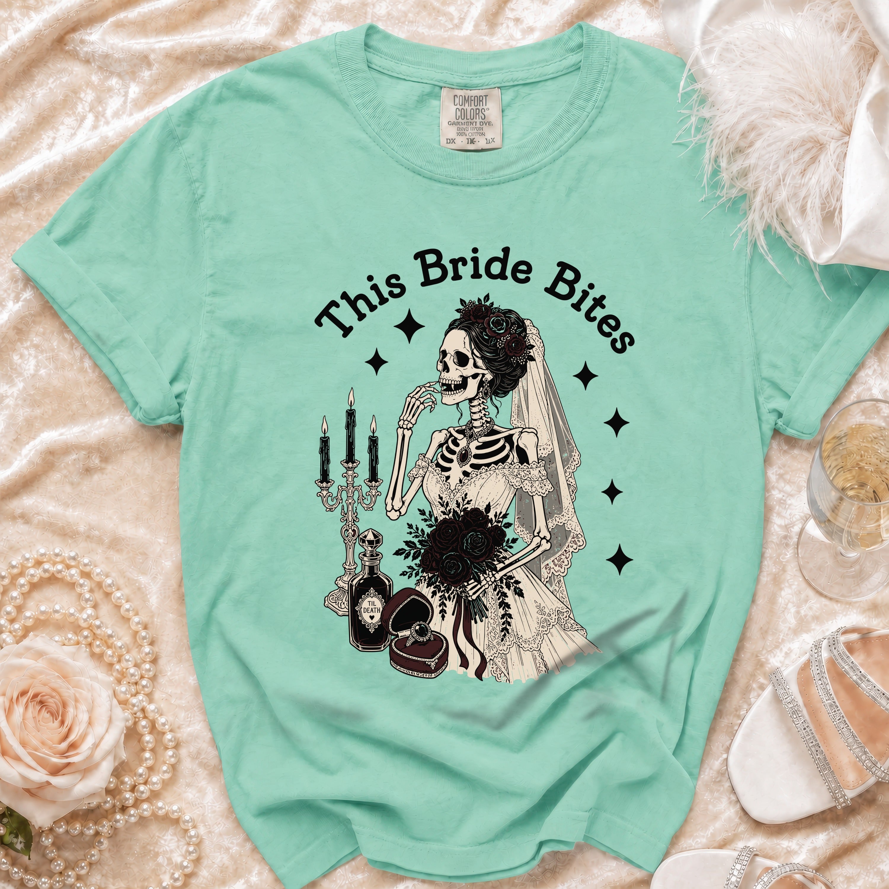 T-shirt with "This Bride Bites" text and a skeleton bride with black roses and wedding items.