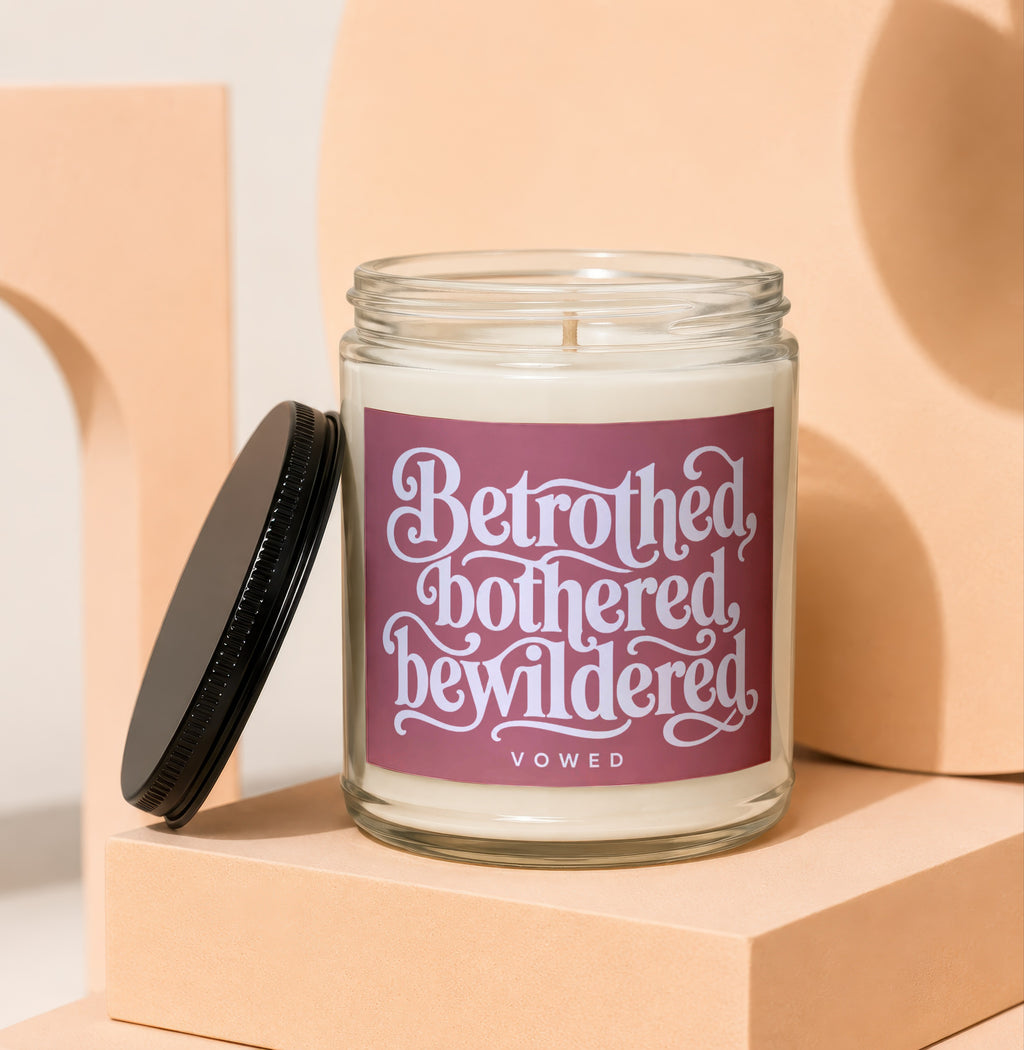 Candle with label "Betrothed, bothered, bewildered VOWED" on a peach pedestal.