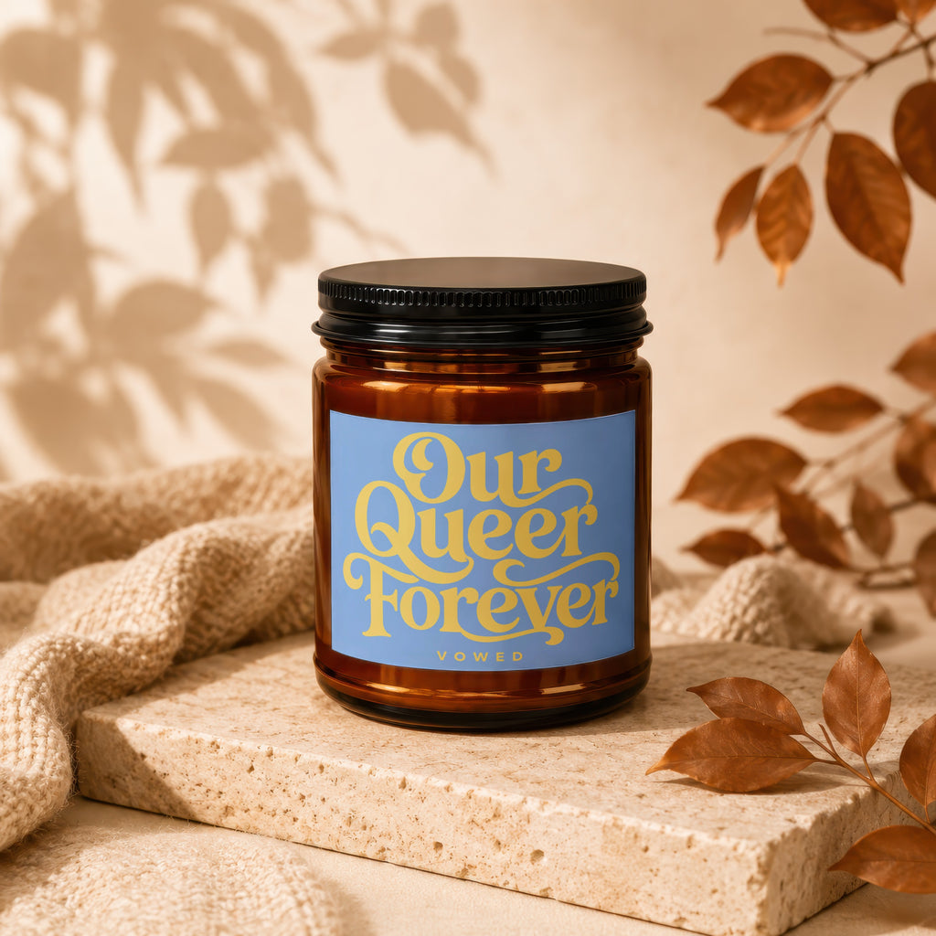 Amber candle with black lid, displaying "Our Queer Forever" text.