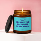 Lit candle in amber jar with teal label reading "I replay the proposal in my head".