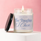 Candle with lit flame on glass jar labeled "Smells Like The Daughter I Chose".