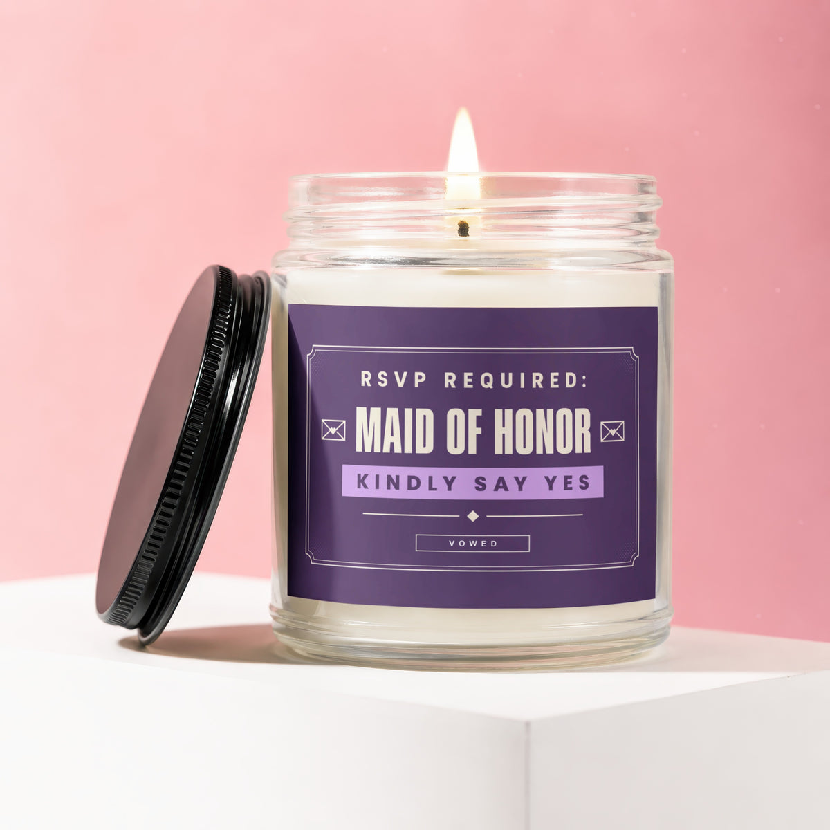 Scented candle with "Maid of Honor" and "Kindly Say Yes" text, lid askew.