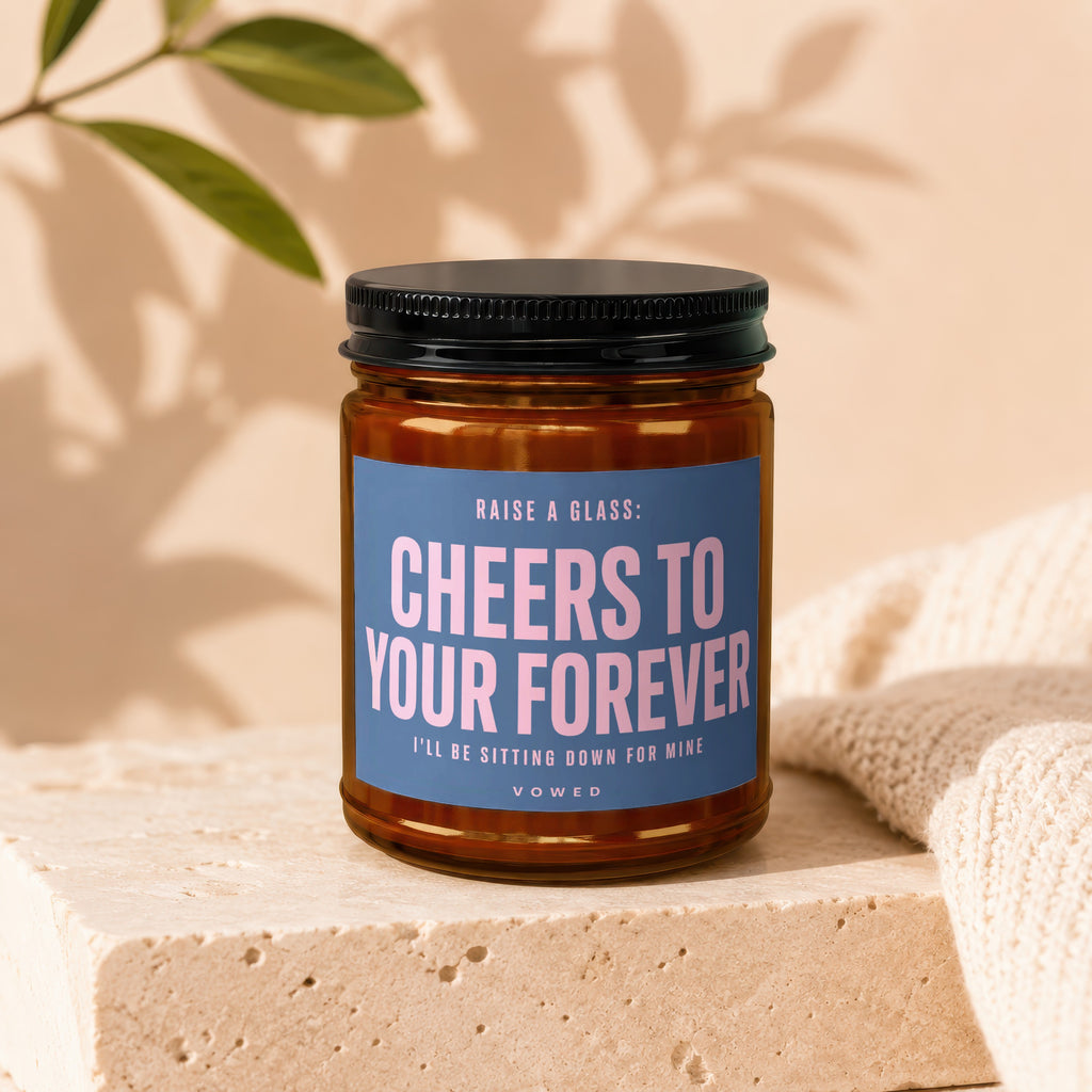 Amber jar candle with blue label saying "Cheers to Your Forever" and "Vowed".
