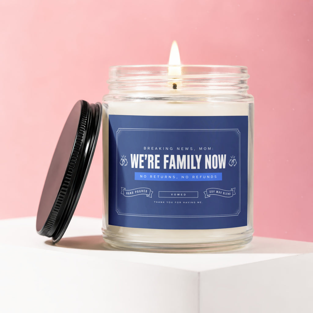 Glass jar candle with "We're Family Now" text, lid off.