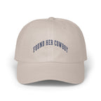 Beige baseball cap with curved dark blue embroidered text reading FOUND HER COWBOY centered on the front panels.